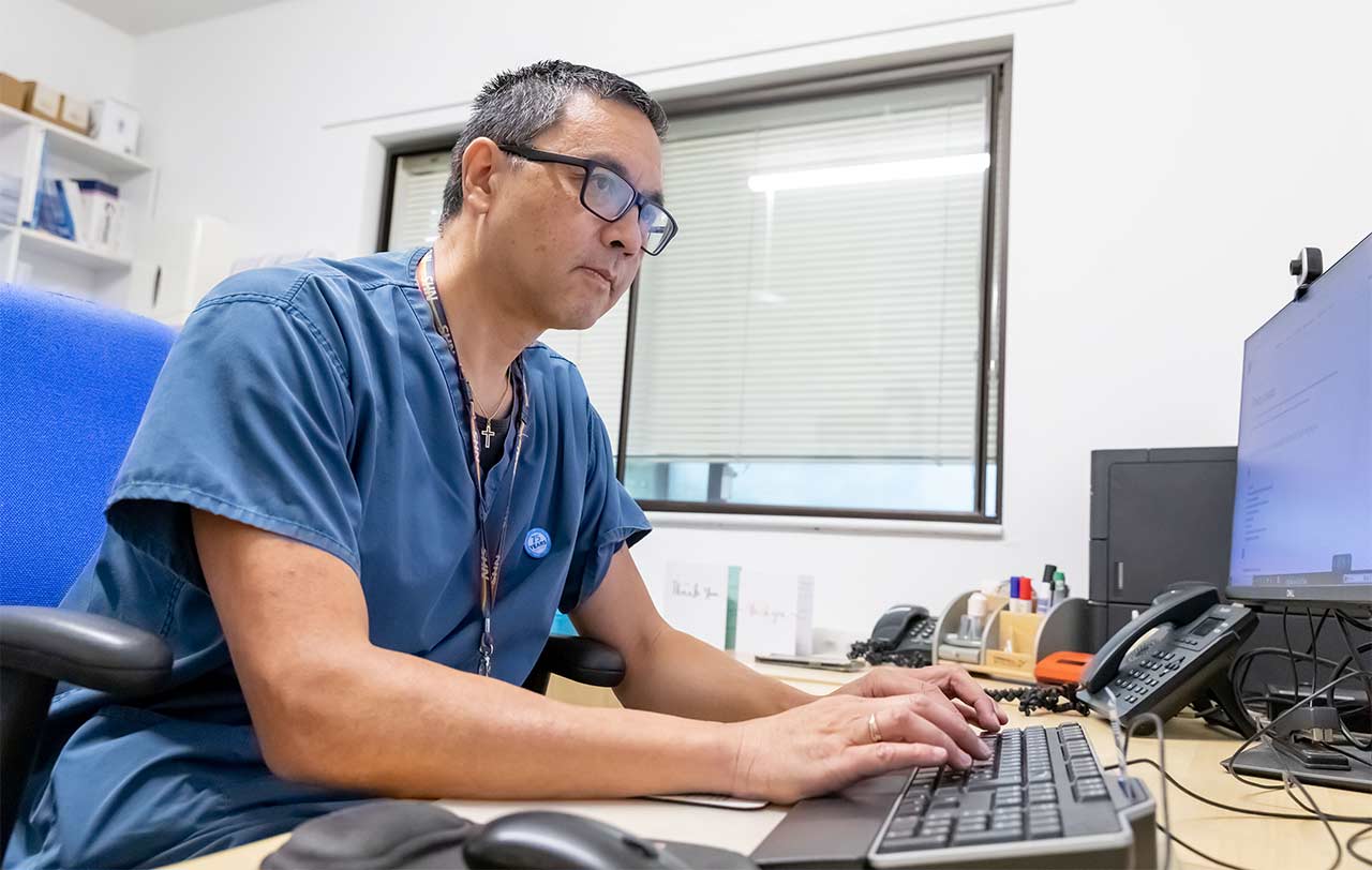 Dr Adrian Hayter, dressed in medical scrubs, works at his computer.