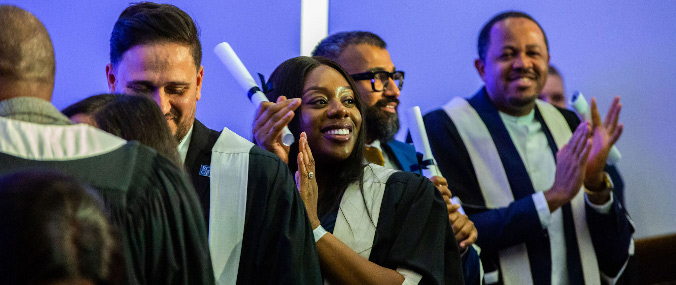A group of graduates clap and cheer in a line wearing robes. 