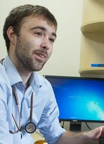 A GP sitting at a desk, speaking to someone off-frame