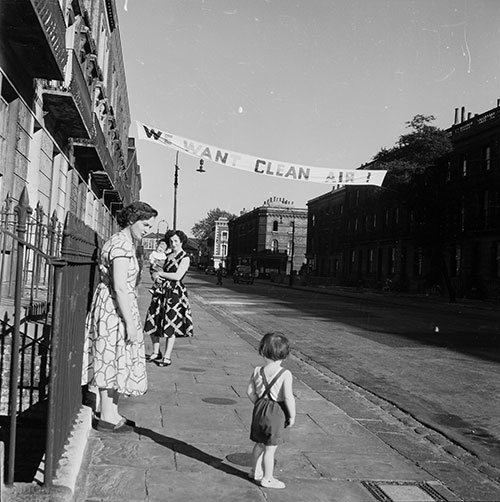 We want clean air protest banner, 1956 (Henry Grant/London Museum)
Black and white photo titled 'We Want Clean Air' showing women and a child on a London street beneath a banner demanding clean air.