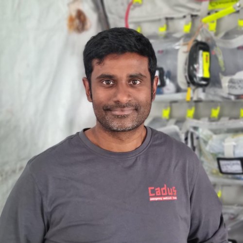 A head and shoulders image of Dr Hareen de Silva wearing a t-shirt in front of a stack of plastic containers.