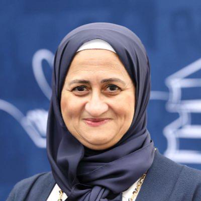 A bright image of Dr Azza Elghonaimy wearing a blue hijab in front of a blue and white background. 