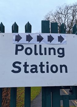 An informal photo showing a paper polling station sign with arrows pointing to the right.