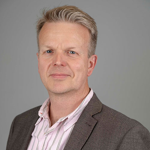 A square head and shoulders photo of Ben Clacy wearing a grey suit.