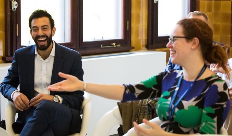 Two GPs sitting in the audience of an event, both laughing. One is gesturing forwards with her arm.