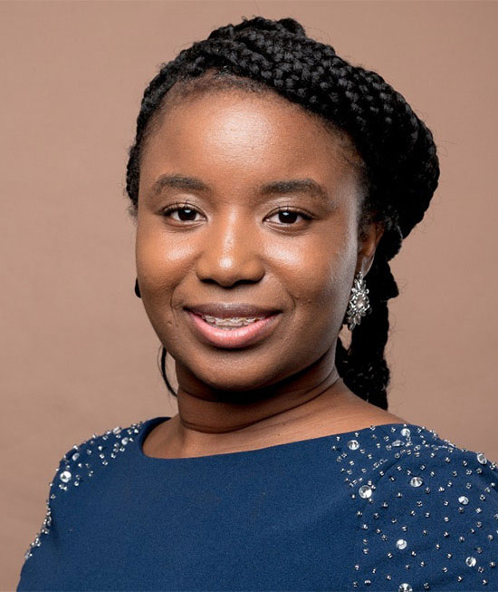 Dr Toyosi Adeniji smiles in front of a terracotta background.