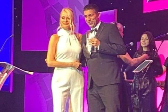 Jaimie Kaffash on stage, standing with a woman and holding a microphone