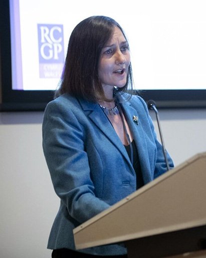 A photo of Dr Rowena Christmas speaking at a lectern wearing a blue jacket.