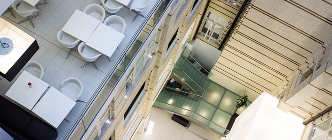 Shot from interior ceiling of 30 Euston Square office building. It shows white tables and chairs on an upper level, and glass effect stairs down to a lower level.