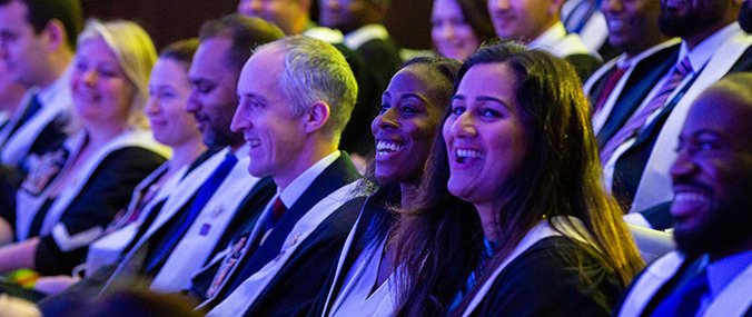 A line of seated GPs at an academic ceremony in a darkened room.