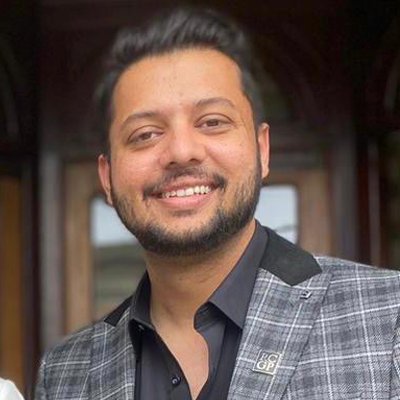 A square image of Dr Akram Hussain smiling outside wearing a check blazer.
