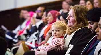 A mother holds her baby in the middle of a seated audience at a professional event
