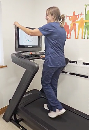 A portrait image of a GP using a treadmill wearing blue scrubs.