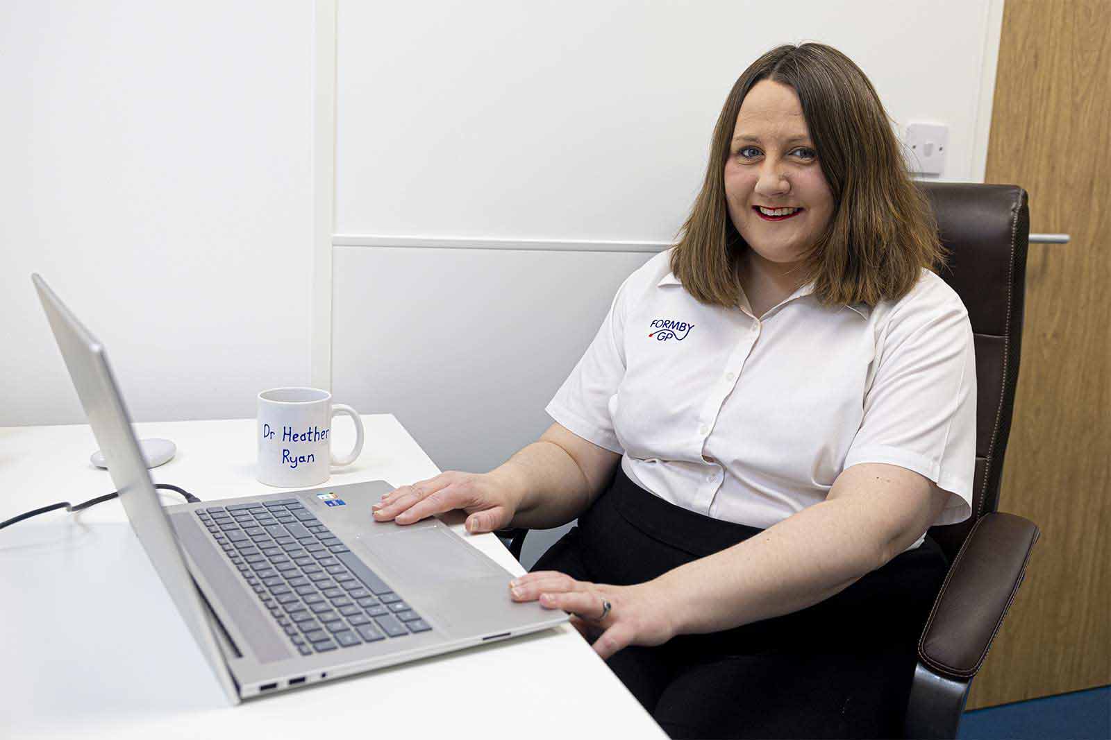 Dr Heather Ryan sits at a white desk with a laptop open in front of her.
